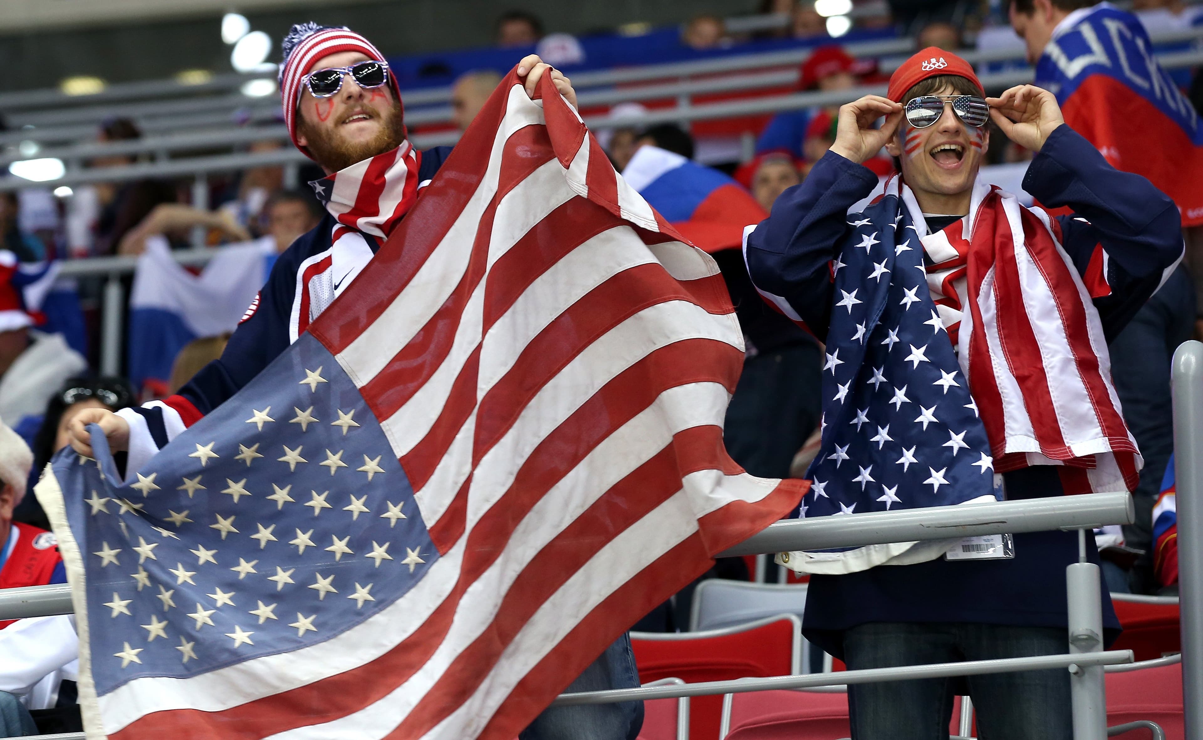 Two Team USA fans with flags wearing sunglasses cheer on athletes.